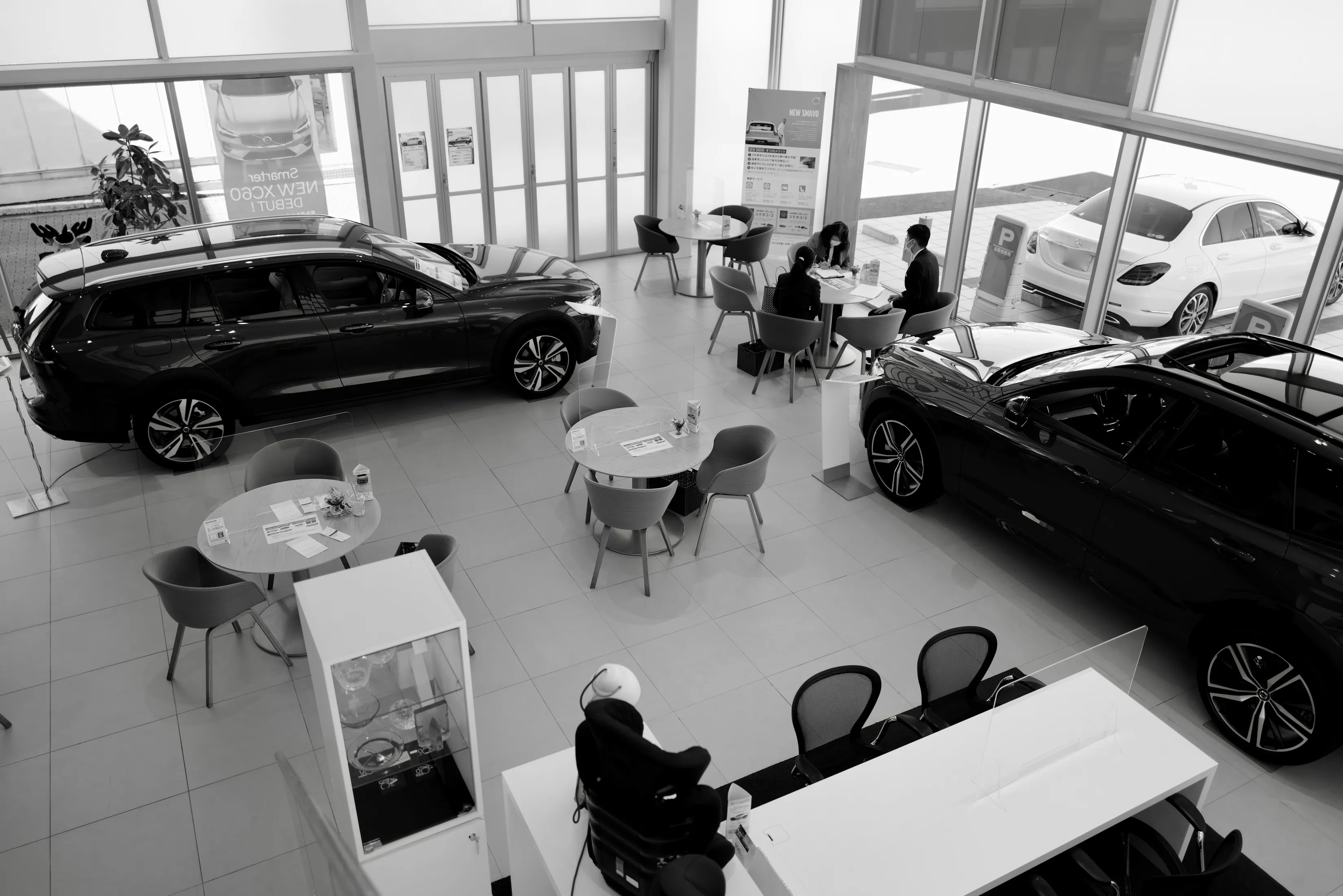 Vista aérea de la sala de exhibición de un concesionario, con autos en exhibición y personas sentadas en las mesas.